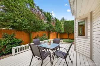 Outdoor dining on the deck set against a backdrop of mature evergreens and full fencing, creating a private setting for grilling, entertaining, and enjoying summer evenings. The layout offers room for multiple uses, from dining to a separate lounging zone.