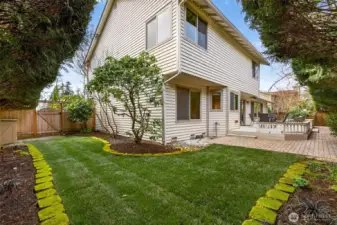 A usable side yard with paver patio space and a grassy area, bordered by established plantings and fencing for privacy. The landscape design keeps maintenance simple while still feeling green and inviting.