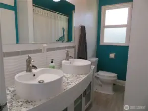 Full bath with two sinks.  A stylish pebble counter and backsplash. Good storage floor to ceiling cabinets to the right.
