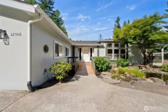 Enjoy the beautifully manicured entryway with no steps—just a gentle ramp leading you into the home. The welcoming path is framed by lush landscaping and a tranquil pond, while large picture windows add curb appeal and fill the interior with natural light.