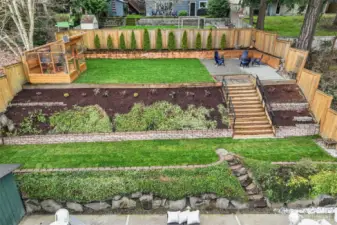 Fully fenced outdoor sanctuary with easy-care landscaping, an expansive levelled terraced backyard, a large patio for entertaining, a gardener's greenhouse, and a storage shed.