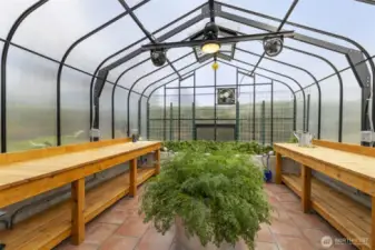 Interior of greenhouse showcasing tile floors, rasied beds and potting bences.
