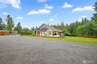 Charming home with expansive deck and large gravel parking area—set on a spacious, fenced lot surrounded by evergreens for privacy and peaceful outdoor enjoyment.