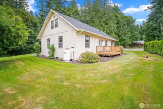 Immaculate side yard with manicured lawn, privacy landscaping, and a secondary deck entrance—offering quiet outdoor space and easy access around the home.