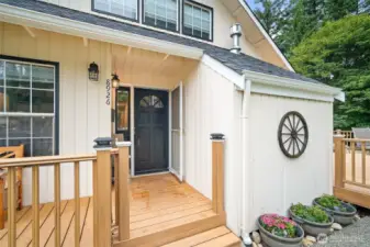 Charming covered entry with warm wood accents, decorative lighting, and colorful flower beds—welcoming you home with a touch of rustic elegance.