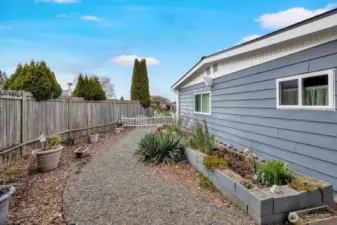 Side yard has gravel walking path. Raised garden bed for herbs, vegies etc. Gardners delight!