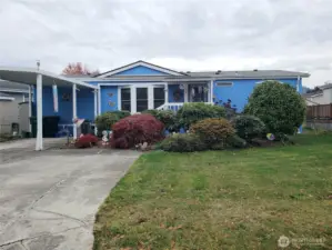 Another Front Picture Showing a Big Yard with Easy Care Landscaping and Carport and Parking Enough for 3 Vehicles.