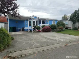 Another Front Picture Showing a Big Yard with Easy Care Landscaping and Carport and Parking Enough for 3 Vehicles.