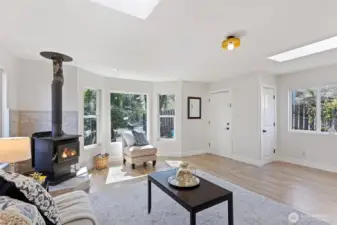 Wood stove on stacked stone, mini-split on the wall, and a south-facing bay window flooding the room with light. A living room built for every season — and looking good doing it.
