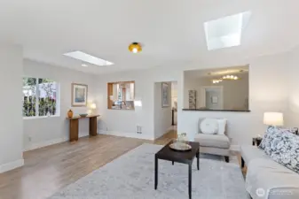 Every opening earns its place: wood-framed serve-through to the kitchen, open-cased passage to the dining room, two skylights overhead. Light moves through this room all day.