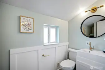 Board-and-batten wainscoting, brass fixtures, round black-framed mirror — the main floor ¾ bath punches above its square footage.