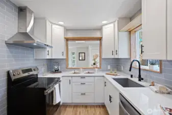 A kitchen reborn — new cabinetry, quartz countertops, blue-grey subway tile, stainless appliances, wall-mount range hood, and a wood-framed serve-through back to the living room.