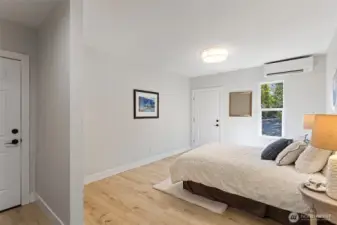 The primary bedroom: mini-split, LVP flooring, and three ways out — driveway, garage, and the exterior storage room.