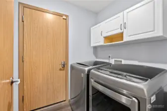 Laundry room offers stainless washer and dryer. Cabinets and shelving and access to the garage.