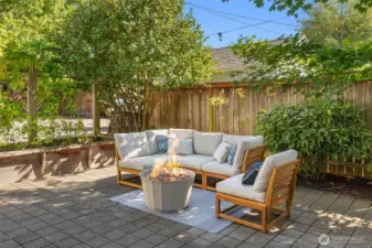 String light lit outdoor room framed by raised beds and evergreen screening.
