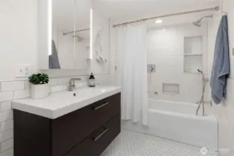 Lower level full bath with soaking tub and shower with built-in niches, sleek storage vanity with LED mirror lighting and classic subway+hex tile palette.