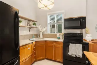 Kitchen appliances include: a stainless steel sink, GE refrigerator, a new  GE electric stove (2024), a drawer style dishwasher with matching wood finish front panel, a Whirlpool microwave (2021) and an InSinkErator garbage disposal. All appliances will remain.