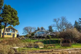 Main house on right, garage/loft studio on left, with beachside picnic area and fire pit in foreground