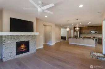 Great room features a beautiful stone faced mantle and fireplace.  Lots of furniture options in this open space.  From this view you can see large kitchen island, primary bedroom to the left and open den ahead.