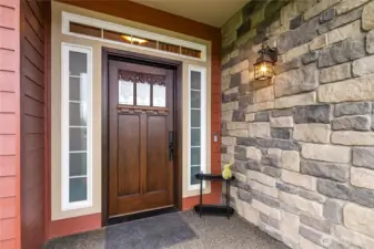 The inviting front porch enhances the home’s Northwest style with stone accents, warm lighting, and striking solid wood door framed by elegant windows.