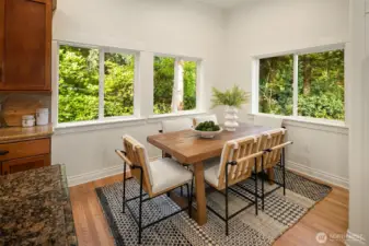 Dining area off kitchen with windows full of trees.
