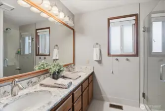 Updated primary bath with dual sinks, quartz counters, tile floors, and a glass-enclosed tile shower.