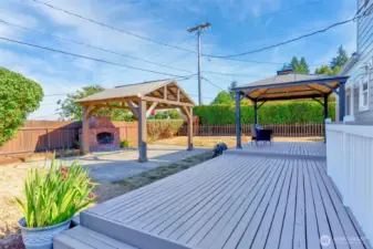 Expansive backyard deck with two gazebo's, outdoor wood fireplace and hot tub on the side of the house