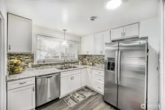 Updated kitchen with white cabinetry, granite countertops, stainless steel appliances, and designer backsplash.