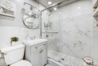 Fully renovated bathroom with glass walk-in shower, marble-style tile, and modern vanity.