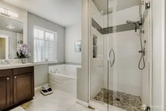 A remodeled walk-in shower has new frameless glass doors, stone tile floor and decorative tile surround with new fixtures.