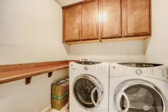 Convenient upper floor utility room with a full-size washer and dryer, shelving and cabinets.