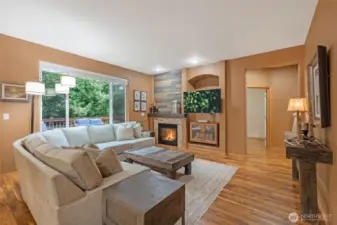 Cozy up in the family room featuring a stunning floor-to-ceiling fireplace with reclaimed wood accents and a rustic mantel. Large picture windows frame peaceful views of the private backyard greenery.