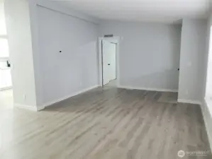 A Different View of the Huge Living Room with New Paint, Trim, Cathedral Ceiling and Vinyl Plank Flooring looking at the Primary Bedroom, Kitchen and Front Door.