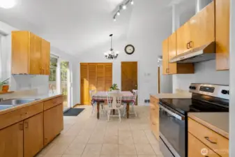 Open kitchen and dining area with vaulted ceiling, ample cabinetry, tile flooring, and direct access to the back deck.