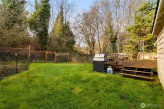 Grassy backyard with deck, grill area, and fenced sections suitable for gardening or pets. Chicken coop included