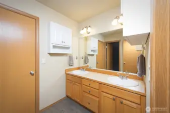 Primary bathroom with dual sinks, shower/tub combo, and laminate flooring.  Door leads to a small room with a window that could be used for maybe a reading room, an office, a second walk-in closet or a storage room.
