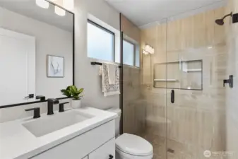 This modern bathroom features a clean layout with a glass-enclosed shower, sleek white vanity, and matte black fixtures for a bold contrast. The neutral tilework and soft lighting create a calm, contemporary space that’s both functional and inviting.