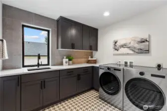 This massive laundry room blends style and utility with sleek cabinetry, a full-size washer and dryer, and generous counter space for folding and sorting. Thoughtful design touches like a built-in sink, patterned tile flooring, and natural light make it both highly functional and visually appealing.