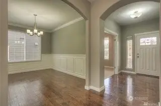 What a lovely entryway with a wide hallway that leads directly into the main floor office. If you’ve been searching for the perfect remote work setup, this office with French doors delivers. Located on the main floor, it features neutral-toned walls, fresh white trim, and a big picture window that lets in natural light while offering a view of the front porch. The soft carpeting and wide slat blinds are the finishing touches that make this space feel calm and organized. And talk about dining with style! High ceilings and crown molding bring that sense of grandeur, while the white wainscoting adds a classic, polished feel. The brushed nickel chandelier lights up the room like it’s hosting a VIP dinner party. And just when you thought it couldn’t get any better, there’s a large closet in the hallway just past the arched entry.