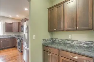 This butler’s pantry is basically the VIP section of your kitchen. With sleek grey, black, and white granite countertops, plus a glass tile backsplash, it’s the perfect place to prep, store, or simply admire. The dark coffee-tone shaker cabinetry with brushed nickel hardware adds a touch of luxury, and the arched doorway leading to the kitchen? A beautiful way to transition from one stunning space to the next.