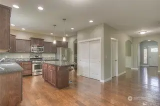 From this angle, you get a peek at the perfect flow of this home. The kitchen is framed beautifully by tall ceilings and stunning hardwood floors, while the pantry closet adds functionality without sacrificing style. The entry to the powder room offers convenience, and the arched doorway to the formal dining room adds just the right touch of elegance. Beyond that, another large arched doorway leads to the entry foyer, completing the open feel of this well-designed space.