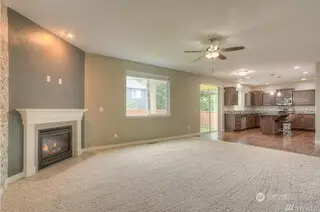 This family room is all about comfort and cozy vibes. The neutral-toned carpeting cuts down on noise, perfect for movie nights when you need that surround sound without the neighbors knowing your entire plotline. High ceilings make the space feel extra roomy, and an arched cutout in the hallway adds a touch of charm as it leads you to the laundry and garage. Across the room, you have the casual dining space in front of the slider, and of course, the kitchen. It is the perfect spot to relax or entertain without missing a beat.