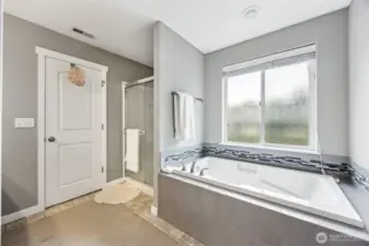 This primary suite bathroom is all about indulgence. The glass door shower is sleek and stylish, while the deep soaking tub sits underneath a large privacy glass window, offering natural light and ventilation when you need it. The wide slat blinds give you control over privacy, while the grey tile surround with a glass tile accent adds a modern touch. With a 5-piece layout, this bathroom has space, style, and all the right features for relaxing after a long day.