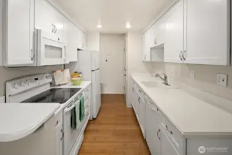 The all-white kitchen inlcludes an electric rang and oven, microwave, refrigerator and dishwasher.