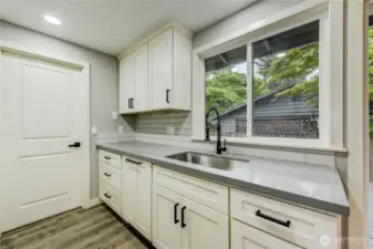 The deep stainless-steel sink with a matte black pull-down faucet sits beneath a sunny window, while the open layout flows seamlessly into the dining area and out to the backyard—ideal for both everyday living and entertaining.
