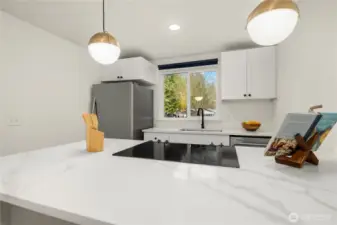 Kitchen with sleek quartz countertops and newer SS appliances. View from bar stool/Dining area on bright kitchen with plenty of daylight streaming in from the kitchen window. What a beautiful view for breakfast!