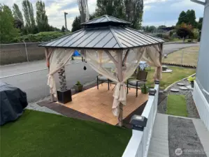 View of fenced backyard with ramp and gazebo.