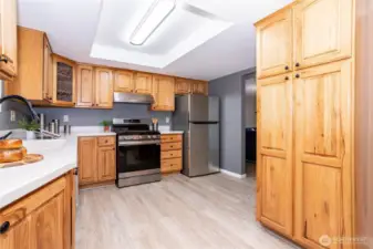 This wide-angle view of the kitchen highlights how functional and approachable the space really is. The natural wood cabinetry brings warmth and a timeless feel, balanced by updated countertops and modern appliances that make daily use easy. The layout offers generous prep space without feeling closed off, allowing multiple people to cook or move around comfortably. Upper and lower cabinet storage is plentiful, keeping everything organized and within reach. The recessed ceiling detail adds subtle architectural interest, while the consistent flooring flowing in from the living areas keeps the home feeling cohesive rather than segmented. It’s a kitchen designed for real life — practical, bright and ready for everything from quick breakfasts to weekend hosting.