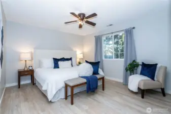 The primary bedroom feels spacious, calm and inviting, with soft natural light coming in through the window. There’s comfortable room for a full bed setup plus additional seating, as staged, without the space feeling crowded. Neutral wall tones paired with updated flooring create a clean, modern backdrop that works with any décor style. The ceiling fan adds both comfort and energy efficiency, while the layout allows for flexible furniture placement depending on your needs. It’s a restful retreat designed for unwinding at the end of the day, offering both scale and comfort without excess.