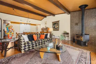 Open-concept living and dining area showcases vaulted pine plank ceilings and a standalone wood-burning fireplace.